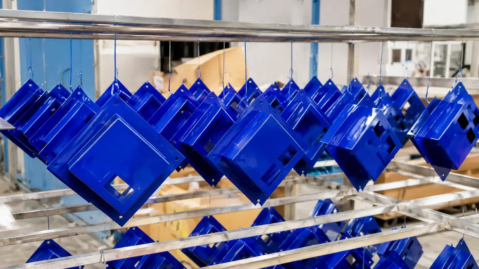 Blue powder-coated steel parts hanging on a finishing line